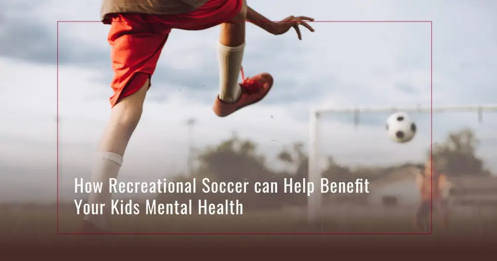 Two kids playing soccer with one kicking a soccer ball into a net