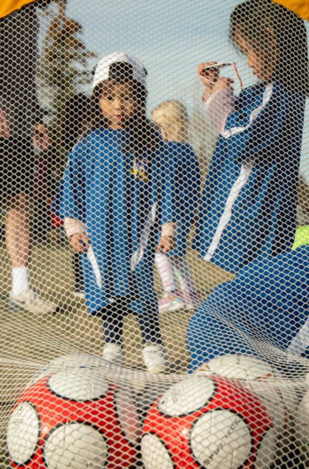 Young girl looking at soccer balls inside a soccer net